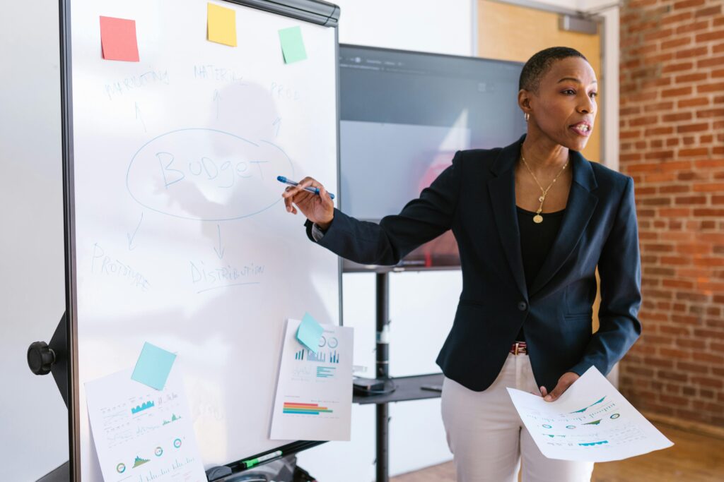 Professional businesswoman POSH Training for Banking Sector explaining budget strategy on a whiteboard during a meeting.